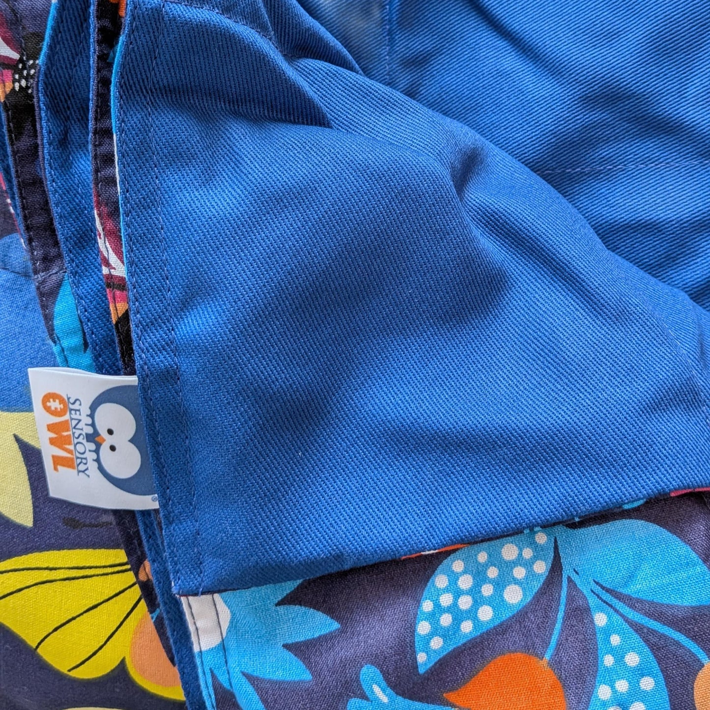 Close-up of a blue fabric with a colorful patterned border and a visible brand label.