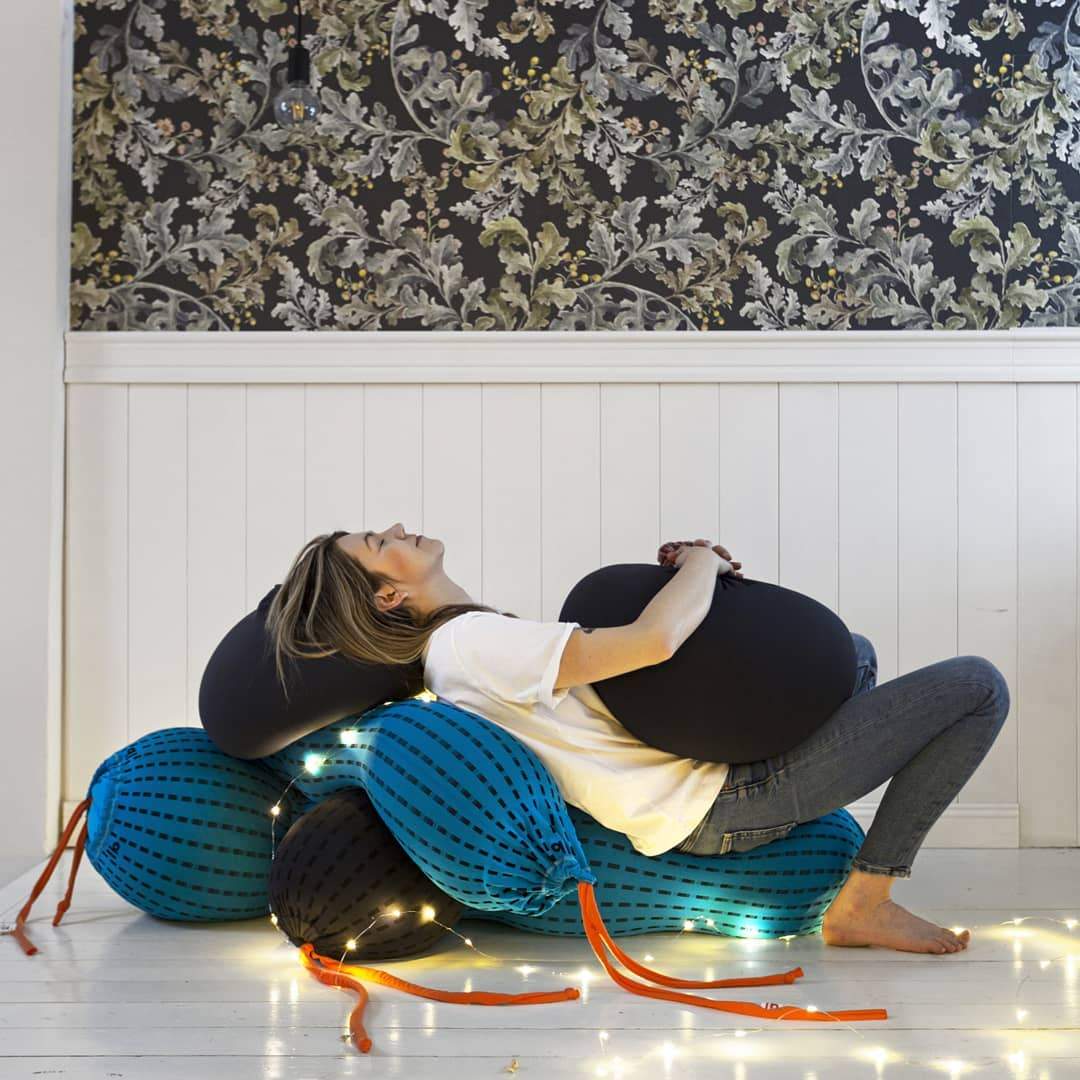 women lying on the pile of human bags and holding black rolling bag